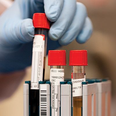 Gloved hand placing full vials into container.
