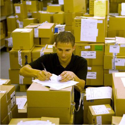 associate in distribution center surrounded by many boxes, writing on paper
