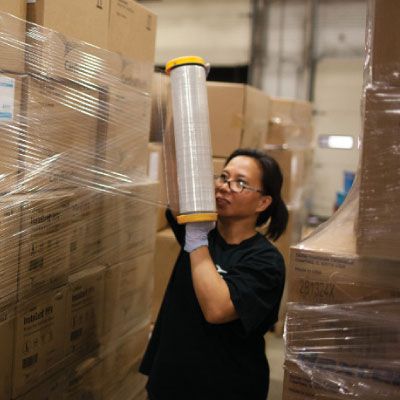 associate at distribution center wrapping pallet of boxes with cellophane