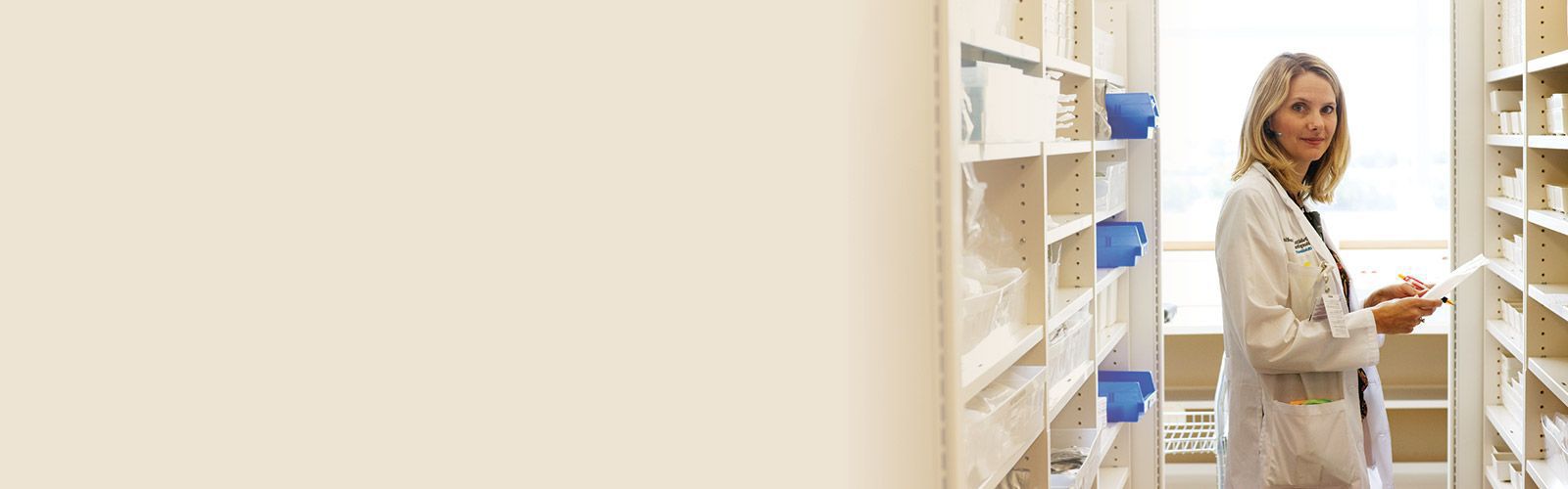 hospital pharmacist with pen and paper in front of pharmacy shelves