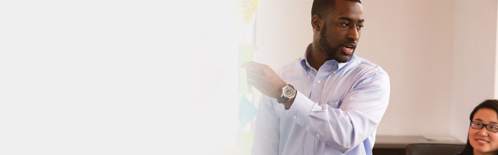 Man adding post-it note to board and talking to people in the room.