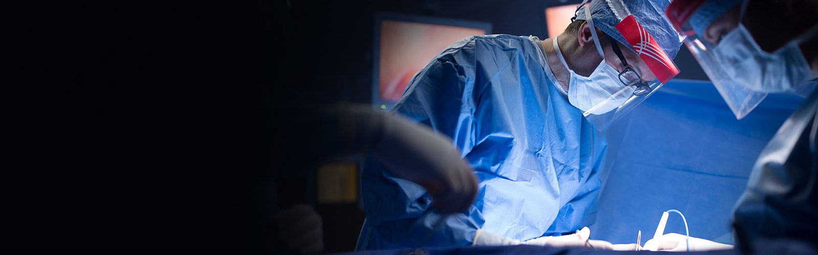 surgeon in full protection performing procedure in dark operating room.
