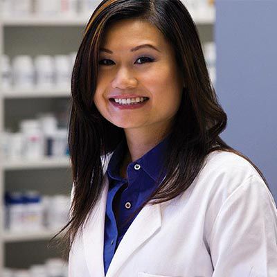 Smiling pharmacist wearing a blue shirt and a pharmacy jacket.