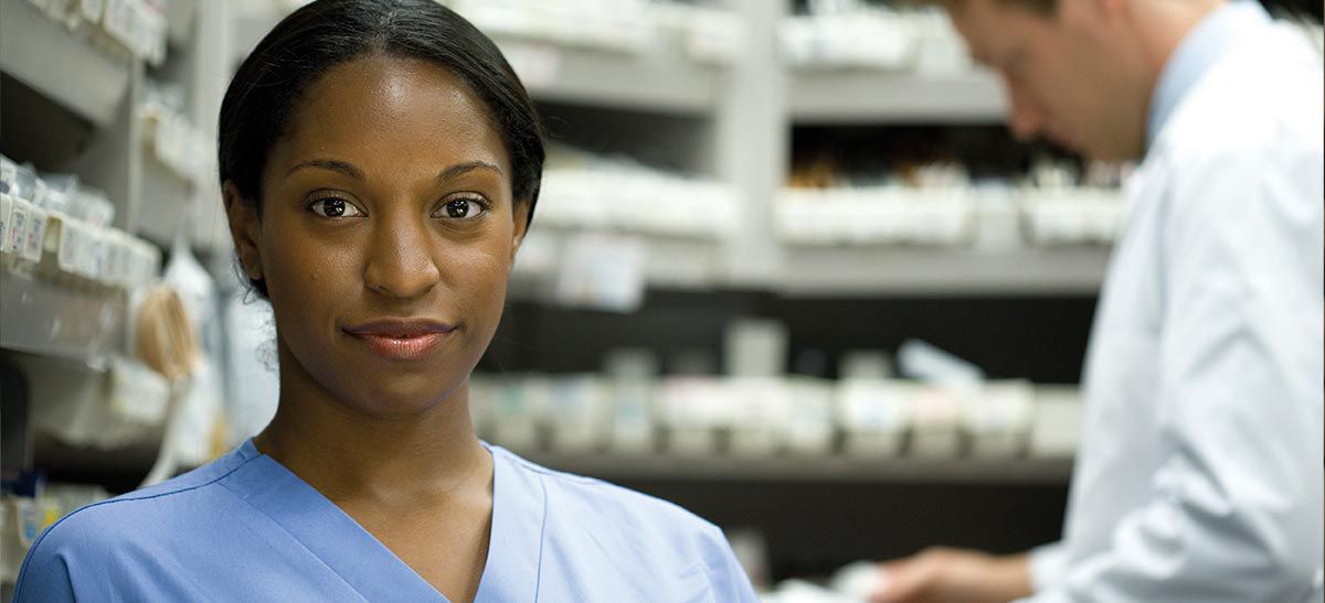 Pharmacist and tech standing in front of pharmacy shelves.