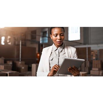 Business woman standing in a warehouse looking at a tablet.