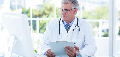 Doctor looking at his computer monitor while holding a clipboard.