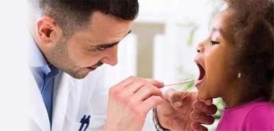 A doctor using a tongue depressor to look into a young patient's mouth.