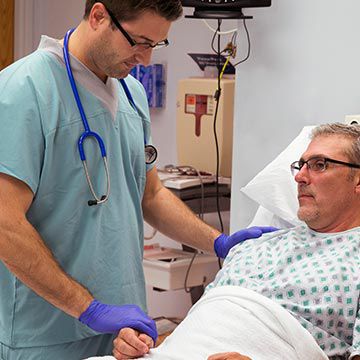 Nurse wearing exam gloves and a stethoscope checking a patient's pulse.