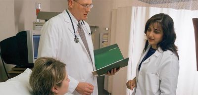 A doctor and pharmacist consulting with a patient bedside.