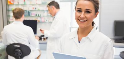 Female pharmacist holding an iPad and two male pharmacists are in the background.